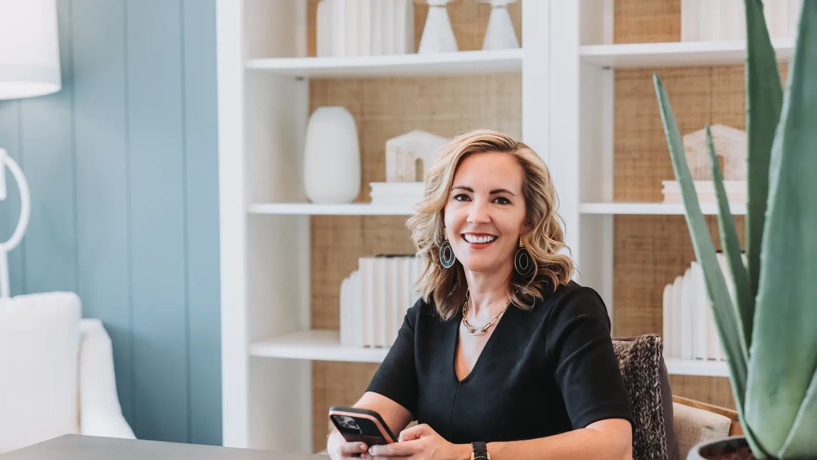 Lucy Thornton at a desk holding her phone, smiling at the camera