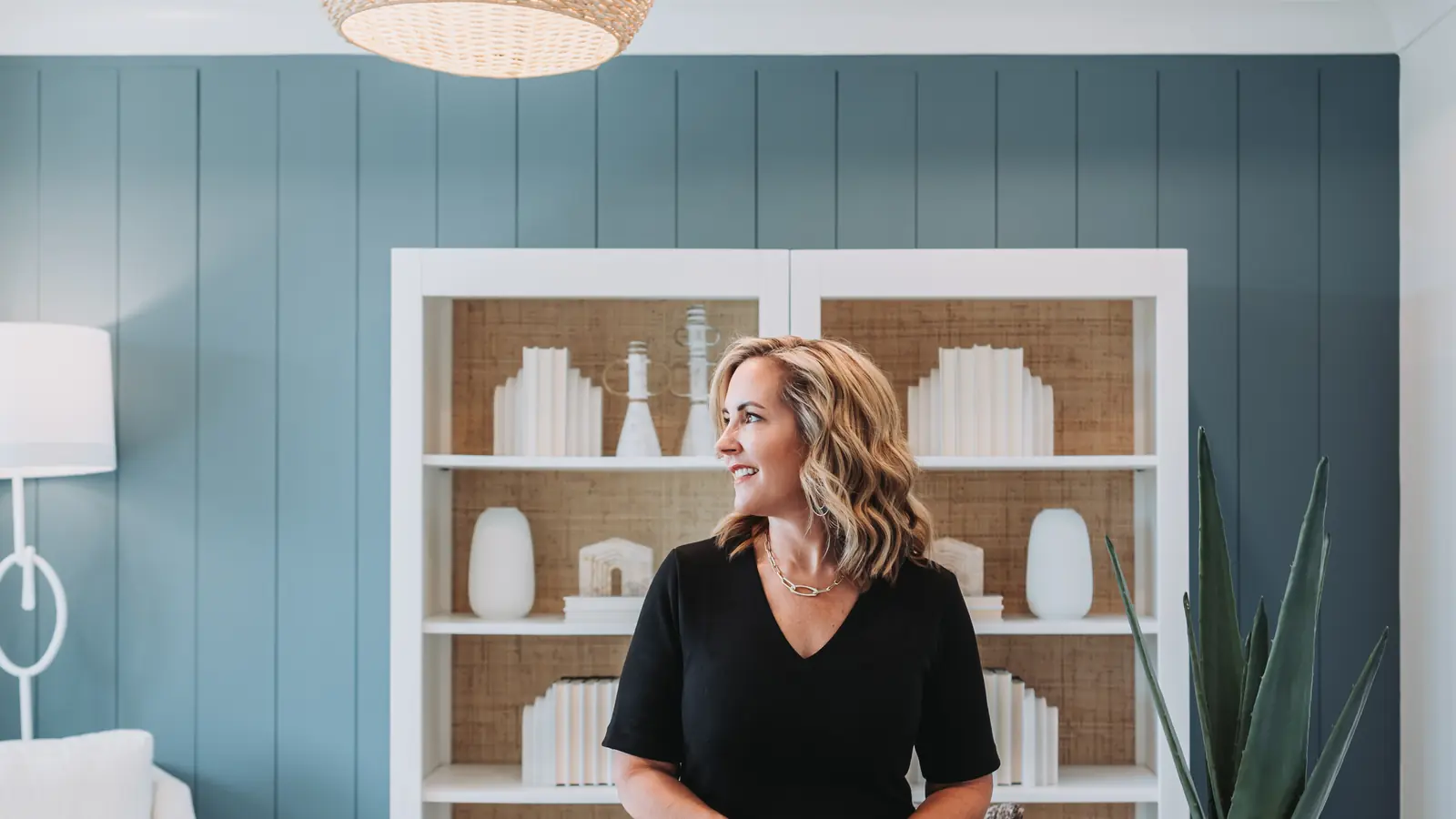 Lucy Thornton sitting on a desk in front of a bookshelf in a blue-panelled office