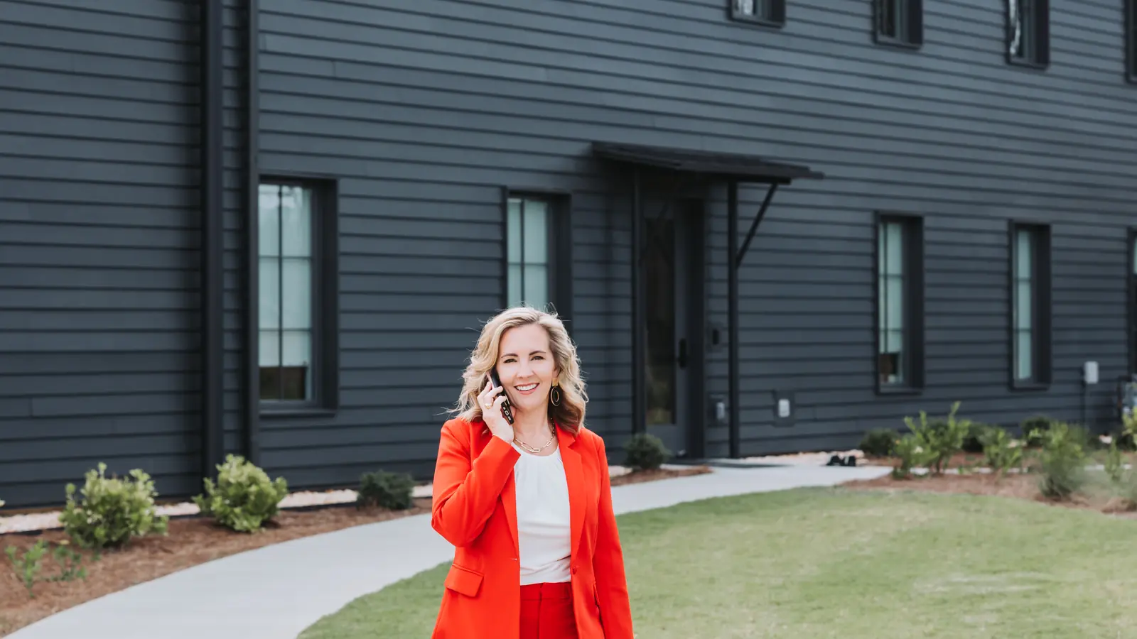 Lucy Thornton in a red suit walking and talking on the phone outside a black modern building