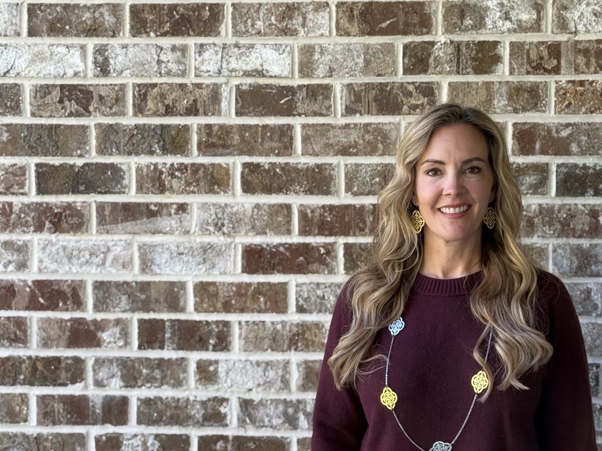 Lucy Thornton smiling in a burgundy sweater in front of a brick wall